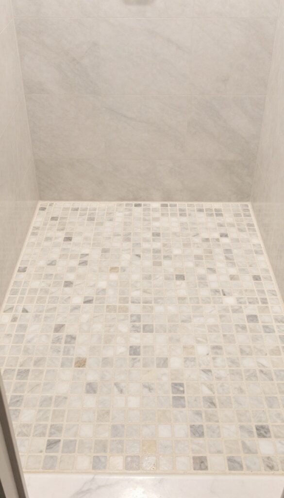 Close-up view of a marble mosaic floor in a walk-in shower, showcasing slip-resistant texture and elegant patterns under bright natural light.