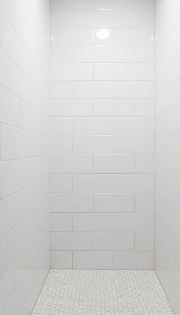 All-white bathroom with layered white tile walls showcasing subway tiles on walls, hexagon tiles on floor, and stacked tiles in shower for visual depth and texture.