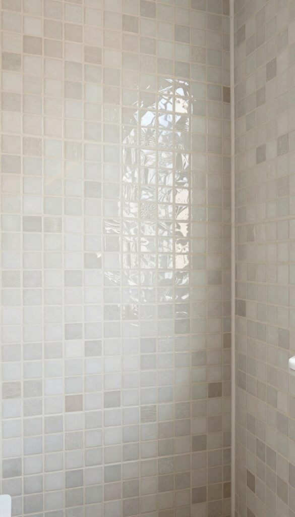 Shower interior with irregular mosaic tiles on a feature wall in bright natural light, demonstrating artistic texture and detail for bathroom decor.
