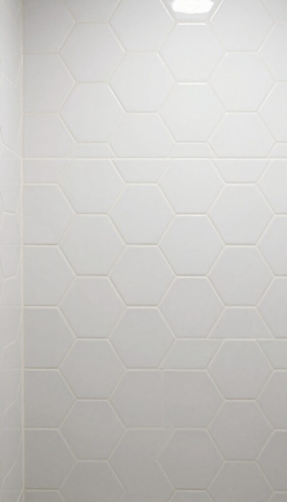 Close-up of a shower wall featuring a mix of hexagon and subway tiles in a vertical strip, showcasing playful geometric contrast with neutral grout and natural lighting.
