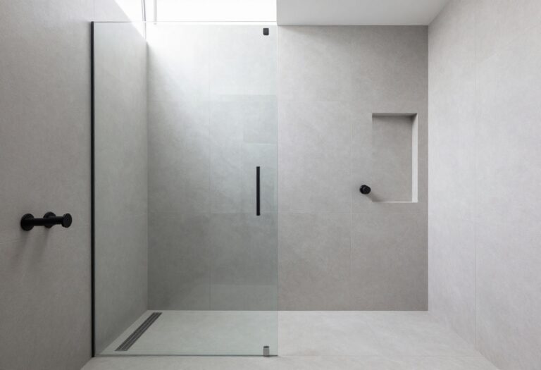 Modern wet shower room with frameless glass enclosure, large gray tiles, matte black fixtures, and natural lighting, highlighting a sleek and streamlined bathroom design.