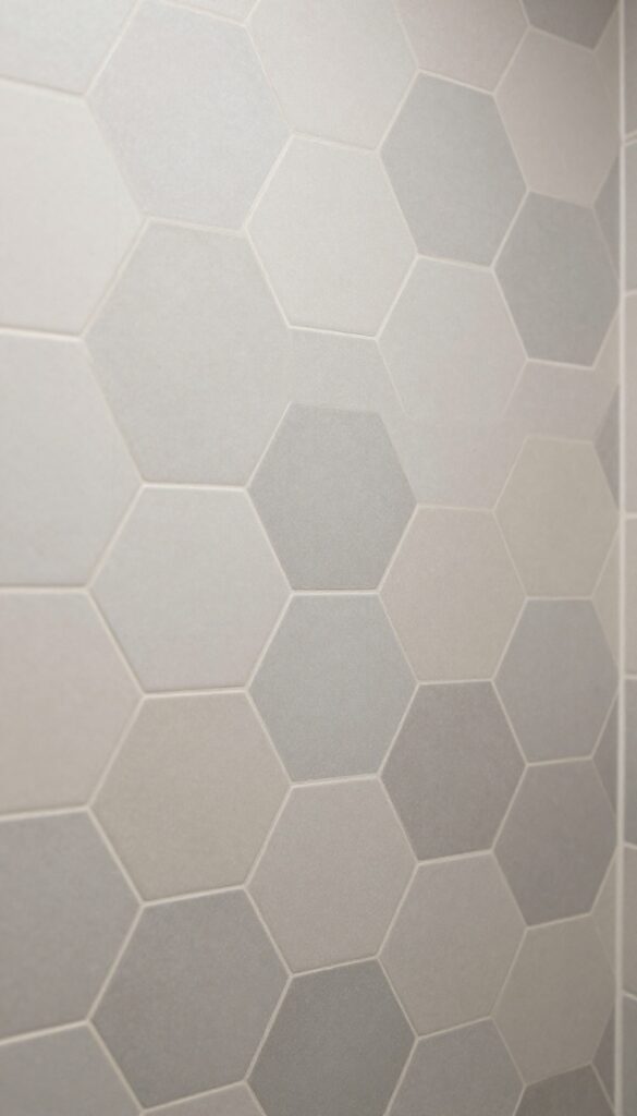 Close-up of hexagon tiles in neutral tones on a shower wall, showcasing geometric pattern and texture in natural light.