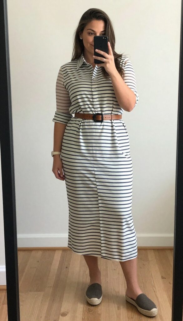 Woman in belted midi shirtdress with rolled sleeves and espadrilles, standing in a bright office or outdoor setting.