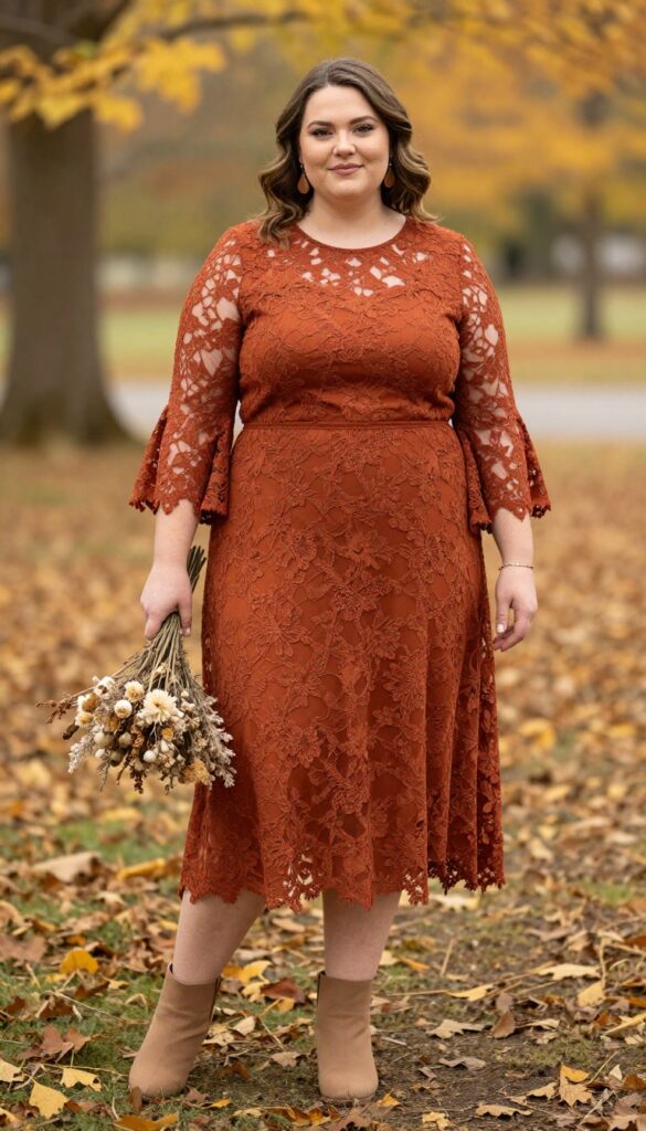 Plus-size woman in rust lace A-line dress with bell sleeves, bronze accessories, tan ankle boots, and dried flower bouquet in outdoor fall setting.