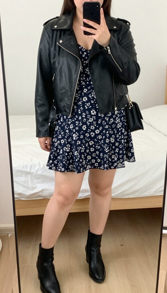 Woman in black leather moto jacket and floral midi dress with ankle boots, crossbody bag, minimal jewelry, mirror selfie.