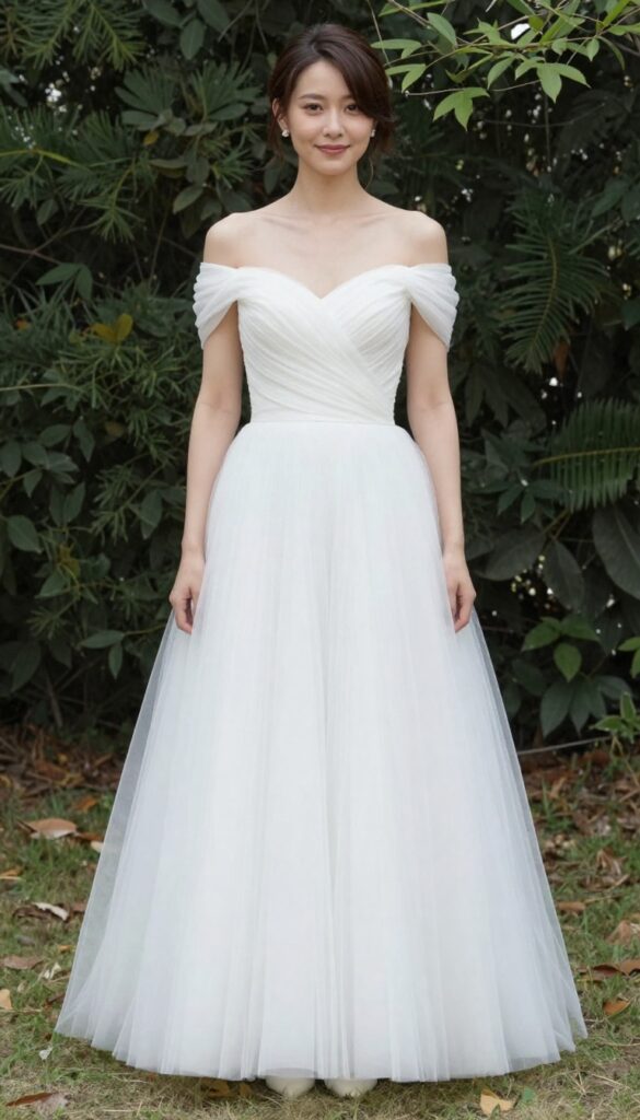 Young adult woman in white puffy wedding dress with bare shoulders and low messy bun, standing in sunlit garden