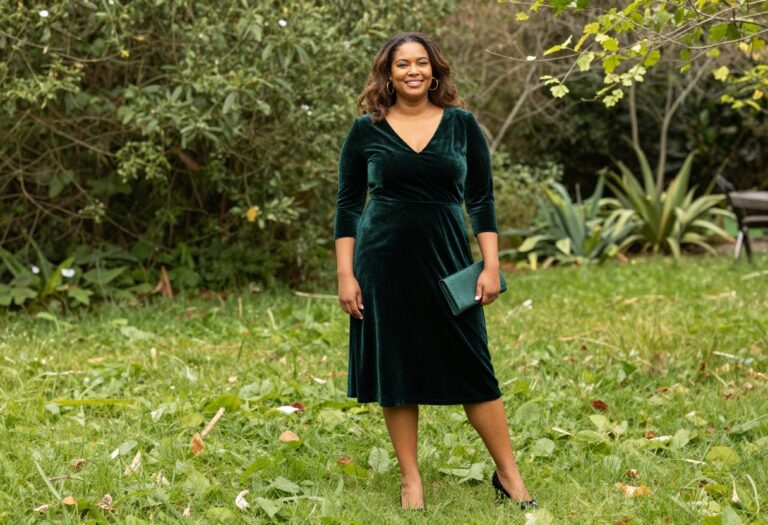 Plus size woman in emerald velvet midi dress with gold accessories in garden
