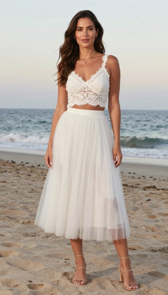 Young woman on beach at sunset wearing white lace crop top and high-waist tulle skirt, elegant and modern bridal look.