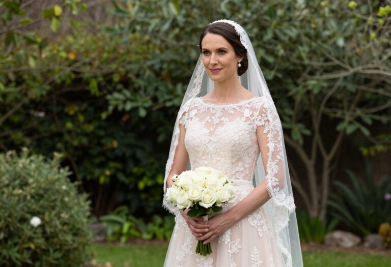 Bride in blush wedding dress with lace veil and pearl earrings in garden