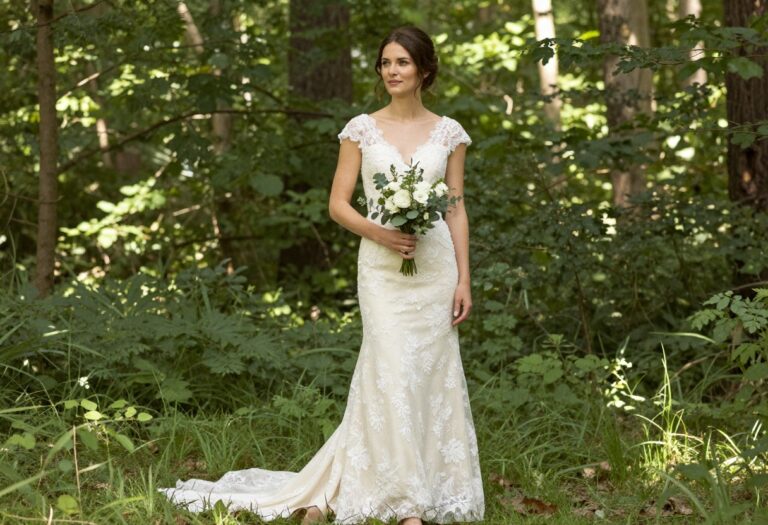 Woman in ivory lace wedding dress with illusion sleeves standing in a forest clearing
