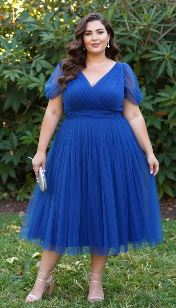 Plus size woman in sapphire blue bishop sleeve tulle dress with metallic clutch and block heel sandals in garden at golden hour