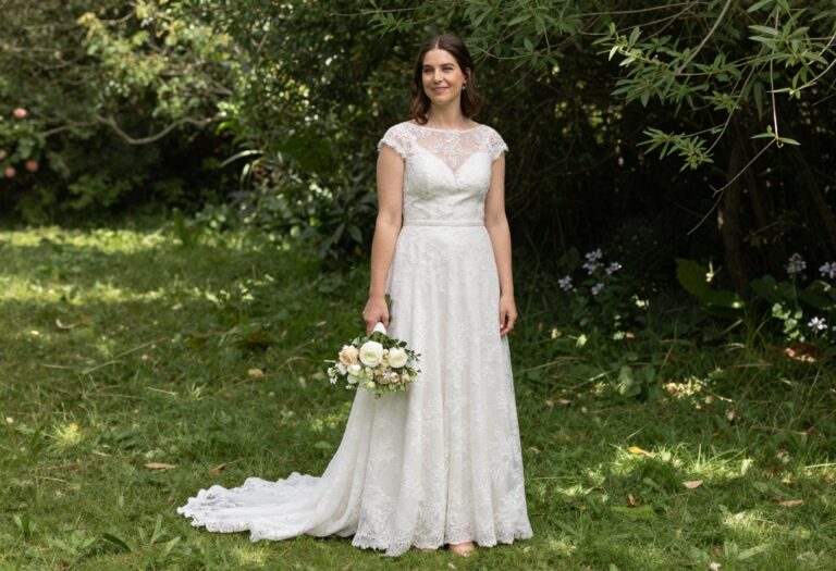 Woman in A-line lace wedding dress standing in garden with bouquet
