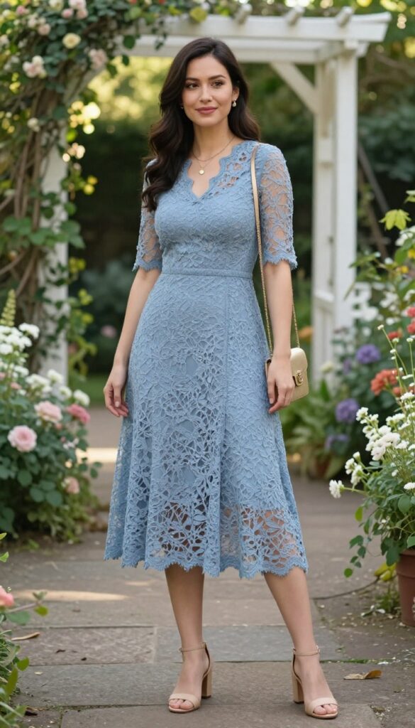 Woman in dusty blue lace midi dress with nude block heel sandals and gold accessories in a garden