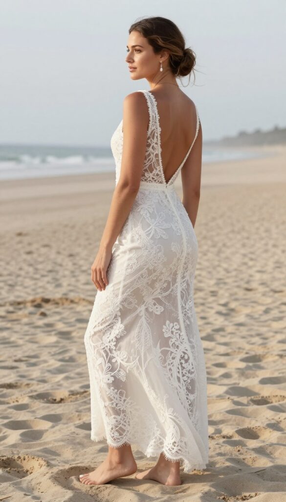 Bride in white lace wedding dress with sheer back, low bun, and backless bra on beach at sunset