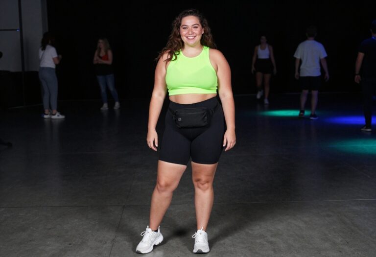 Plus size woman in neon green mesh crop top and black bike shorts posing under UV lights at a rave