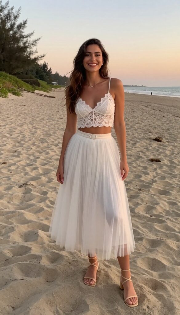 Young woman in white lace crop top and high-waist tulle skirt at beach wedding sunset