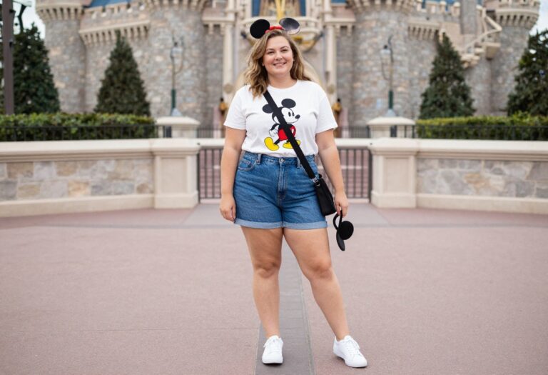 Plus-size woman in Mickey tee and denim shorts at Disney Castle
