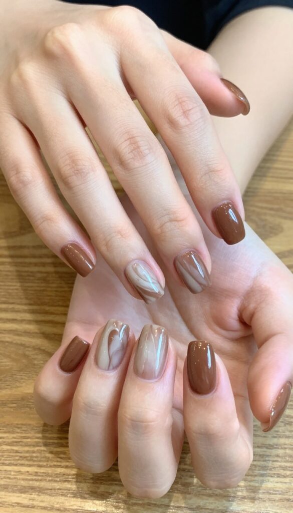 Mocha swirl nails with glossy brown base and creamy beige swirls on rounded almond shaped nails