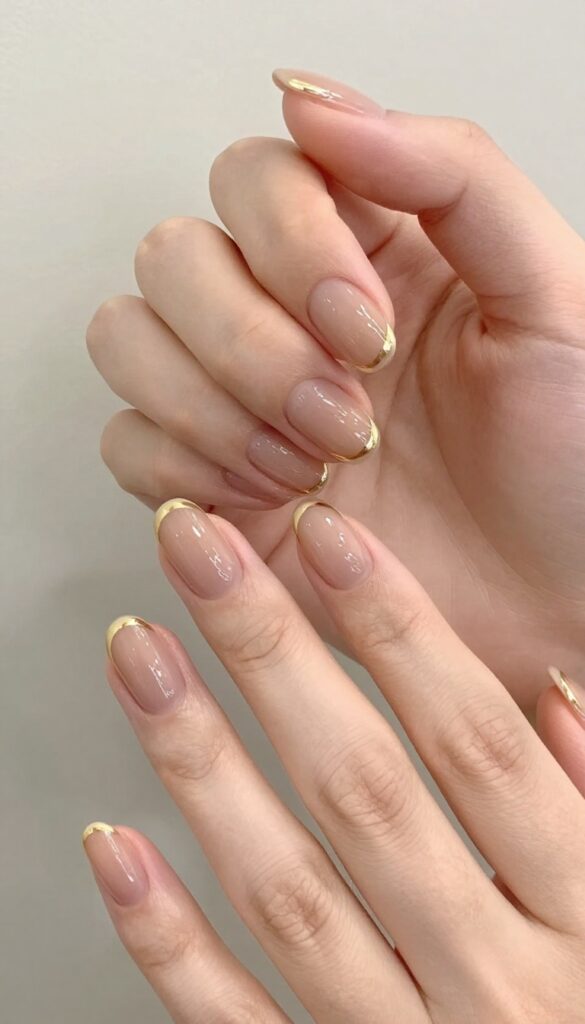 Short almond nails with sheer nude base and metallic gold stripe