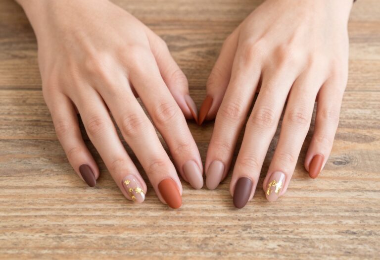 French fall nail ideas with almond-shaped nails in matte terracotta and chocolate tones with gold foil accents on a rustic wooden surface