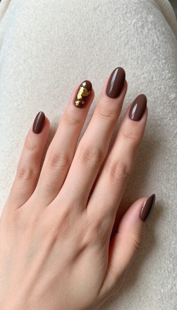 Matte brown nails with gold foil accents on a woman's hand