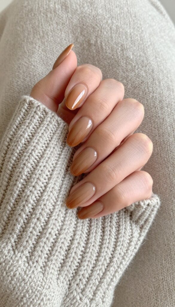 Toasted almond gel manicure on almond-shaped nails with glossy finish, resting on a knit sweater