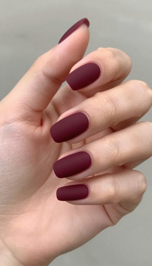 Burgundy matte nails with negative space crescent cutouts on almond-shaped nails
