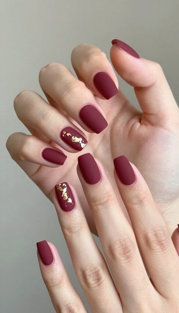 Short almond nails with matte merlot polish and gold foil accents