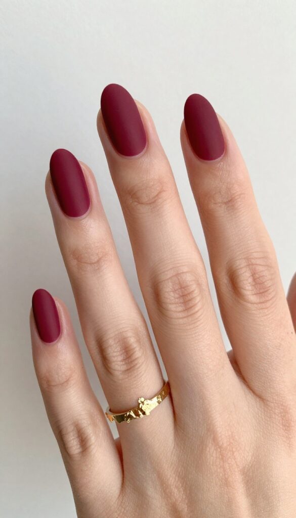 Matte merlot nails with gold foil accents on ring finger