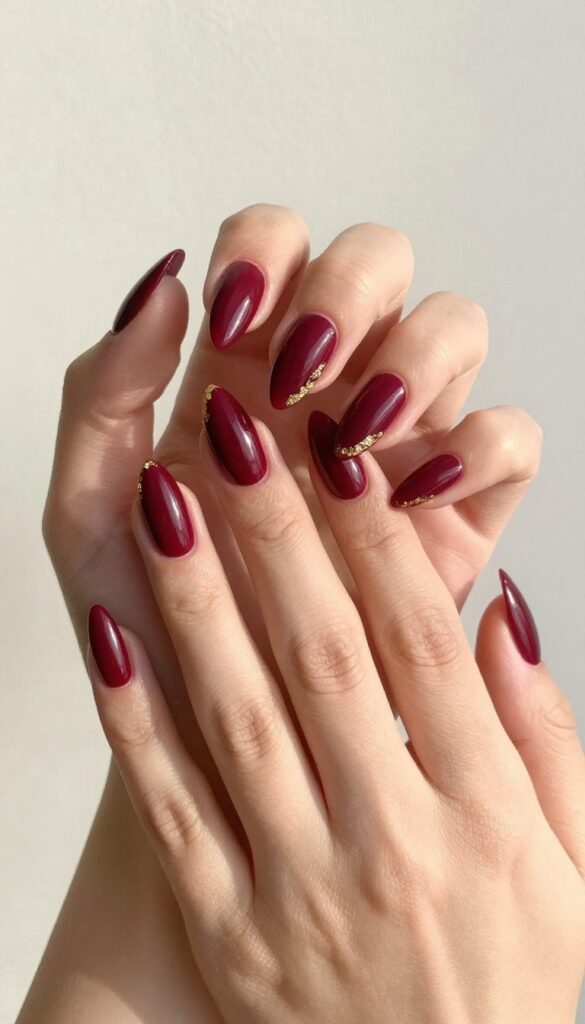Burgundy stiletto nails with gold foil accents on a woman's hand