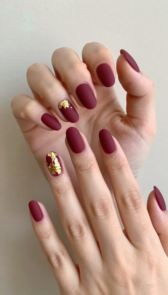 Matte merlot nails with gold foil accents on ring finger and thumb