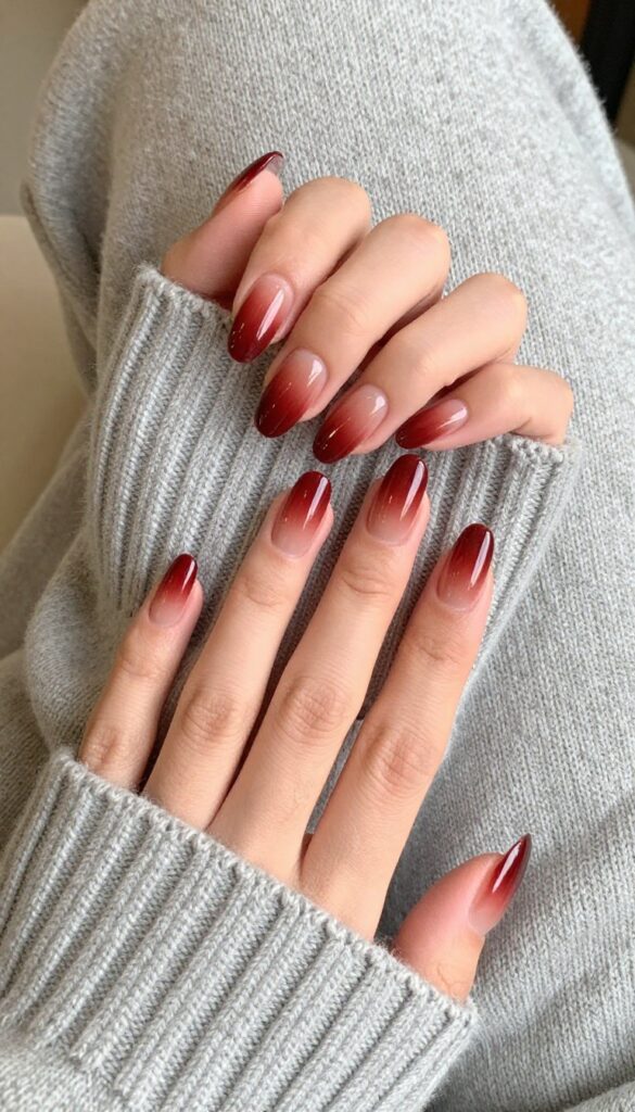Oxblood ombré nails on almond-shaped nails, gradient from dark to sheer, posed on a sweater