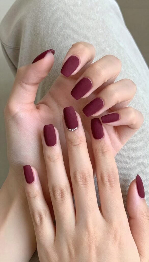 Matte burgundy coffin nails with single rhinestone accent on ring finger