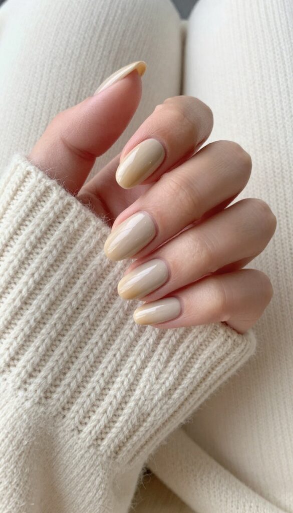 Almond-shaped nails in toasted almond milk beige polish with glossy finish on a cream sweater