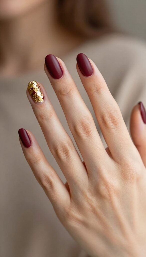 Short almond nails in matte merlot with gold foil accents on ring finger