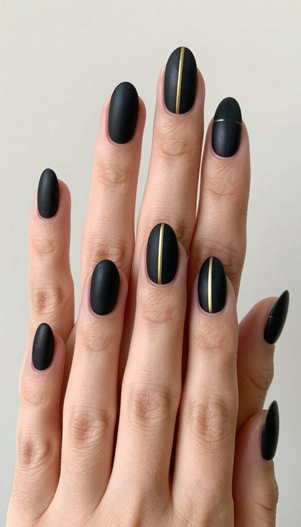 Matte black nails with a single gold stripe down the center, short almond shape, minimalist fall manicure