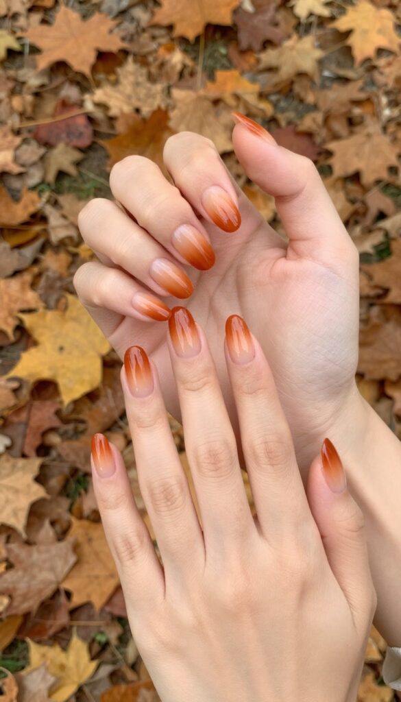 Burnt orange ombré nails with nude base, almond shape, glossy finish