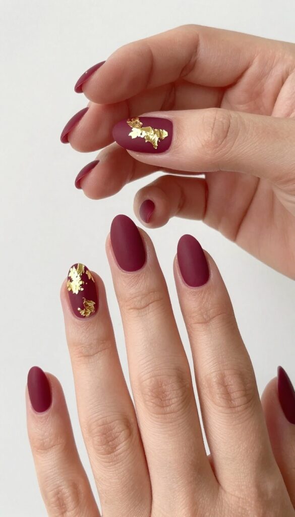 Matte merlot nails with gold foil accents on almond shape