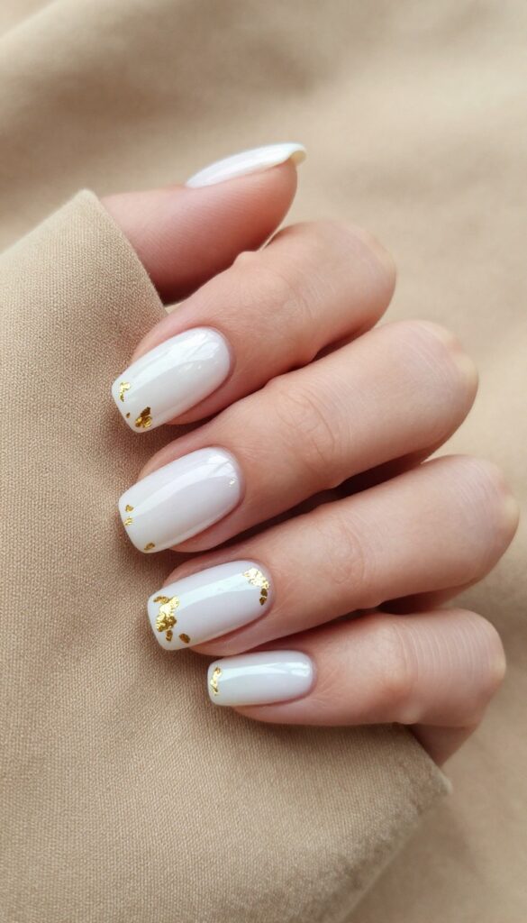 Short pearlescent white nails with gold foil accents on a woman's hand