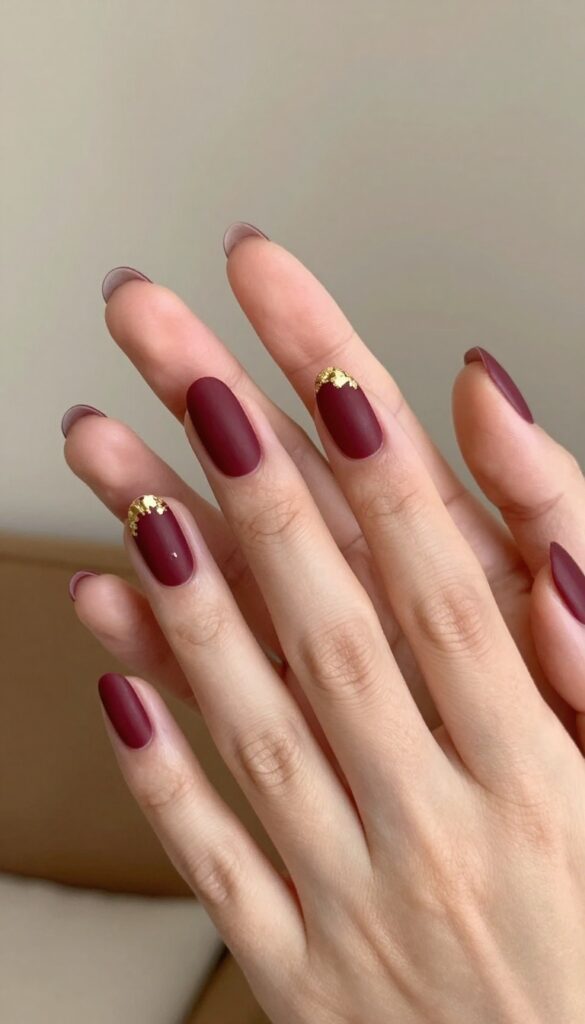 Matte merlot nails with gold foil accents on almond-shaped nails