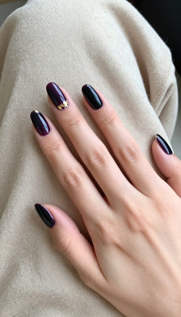 Deep plum nails with gold foil accents on almond shape