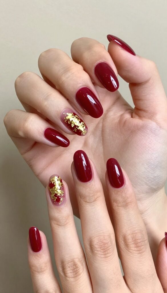 Cranberry nails with gold foil accents on almond-shaped nails