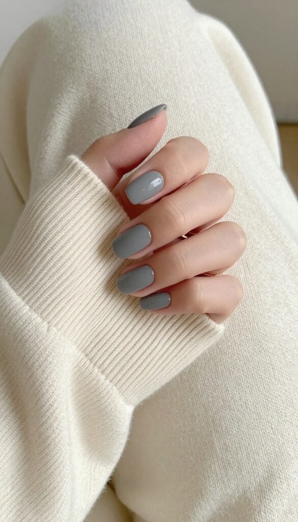 Smoky grey matte nails on short rounded nails, resting on a cream knit sweater with a gold ring