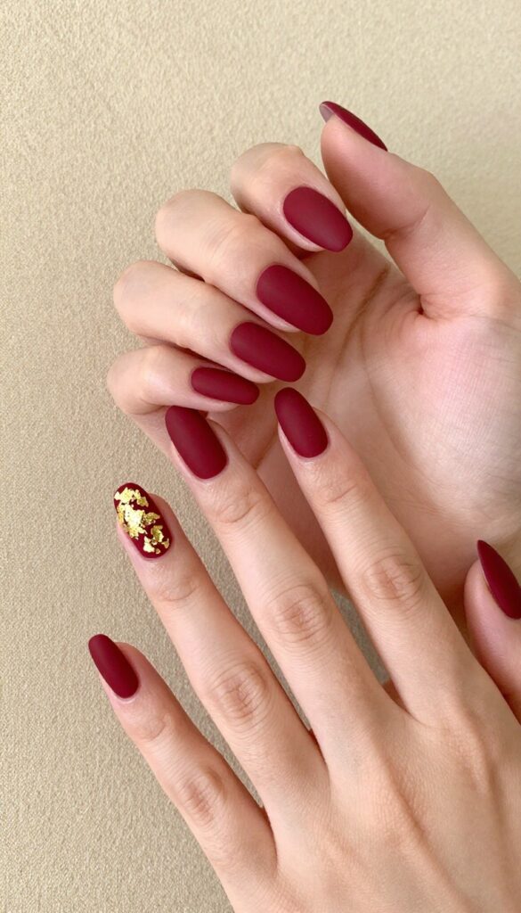 Matte merlot nails with gold foil accents on almond-shaped nails