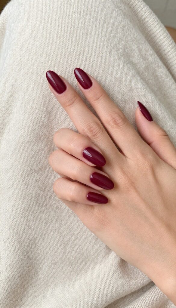 Matte merlot dip powder nails on almond-shaped nails, resting on a chunky sweater