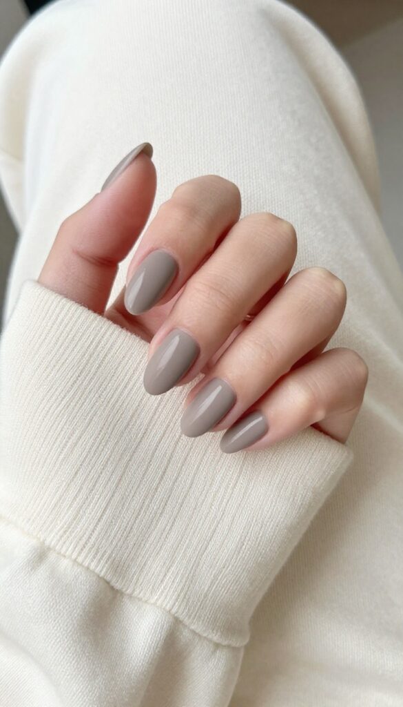Almond nails in smoky taupe polish with matte finish on a woman's hand resting on a cream sweater