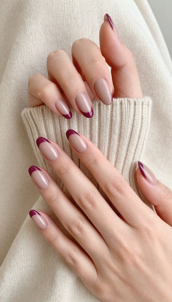 Matte berry French tip nails on almond-shaped nails with a sheer nude base and deep plum matte tips, resting on a sweater.