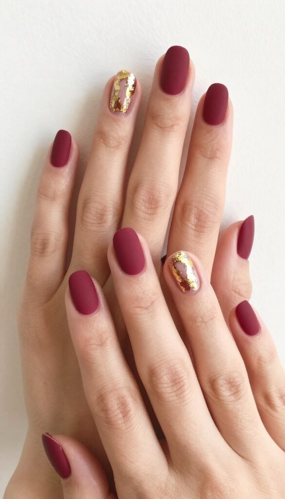 Matte bordeaux nails with gold leaf accents on two nails, medium squoval shape, autumn manicure