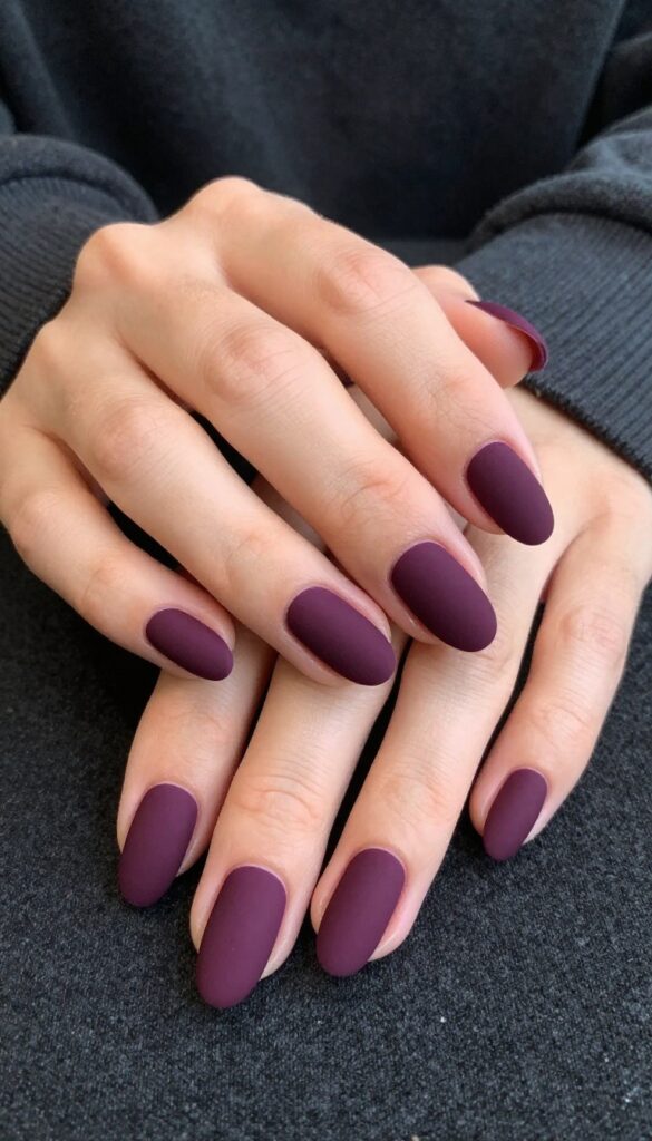 Midnight plum velvet matte nails on almond-shaped nails, resting on dark fabric