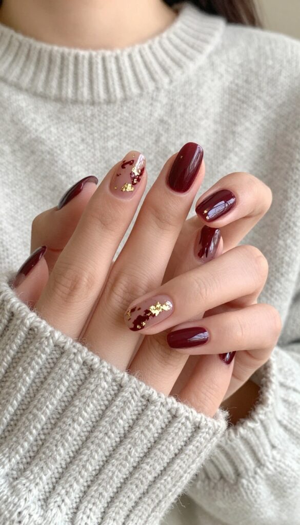 Velvet burgundy nails with gold foil accents on almond-shaped nails